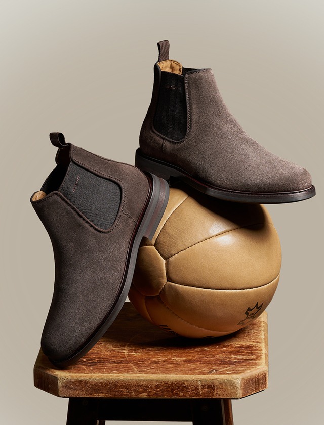 Braune Stiefeletten stehen auf einem Fußball, der auf einem Holzstuhl platziert ist.