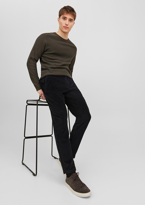 Ein junger Mann sitzt auf einem Hocker, trägt einen grünen Pullover und schwarze Hose. Ein junger Mann sitzt auf einem Hocker, trägt einen grünen Pullover und schwarze Hose.