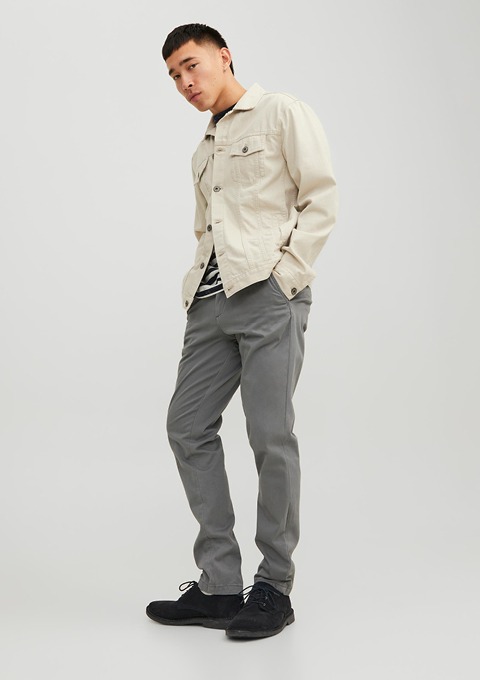 Ein Mann trägt eine beige Jacke, gestreiftes T-Shirt und graue Hose. Er steht aufrecht mit einem neutralen Gesichtsausdruck. Ein Mann trägt eine beige Jacke, gestreiftes T-Shirt und graue Hose. Er steht aufrecht mit einem neutralen Gesichtsausdruck.