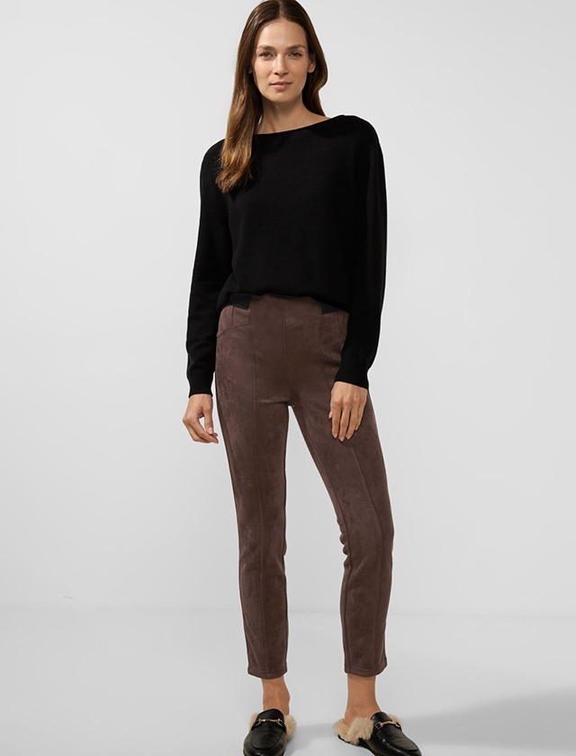 Eine Frau trägt einen schwarzen Pullover und braune Hosen. Sie steht vor einem neutralen Hintergrund. Eine Frau trägt einen schwarzen Pullover und braune Hosen. Sie steht vor einem neutralen Hintergrund.