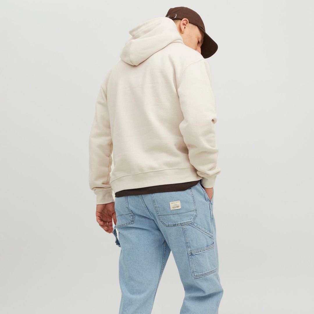 Eine Person trägt einen beigefarbenen Kapuzenpulli und hellblaue Jeans, von hinten aufgenommen. Eine Person trägt einen beigefarbenen Kapuzenpulli und hellblaue Jeans, von hinten aufgenommen.