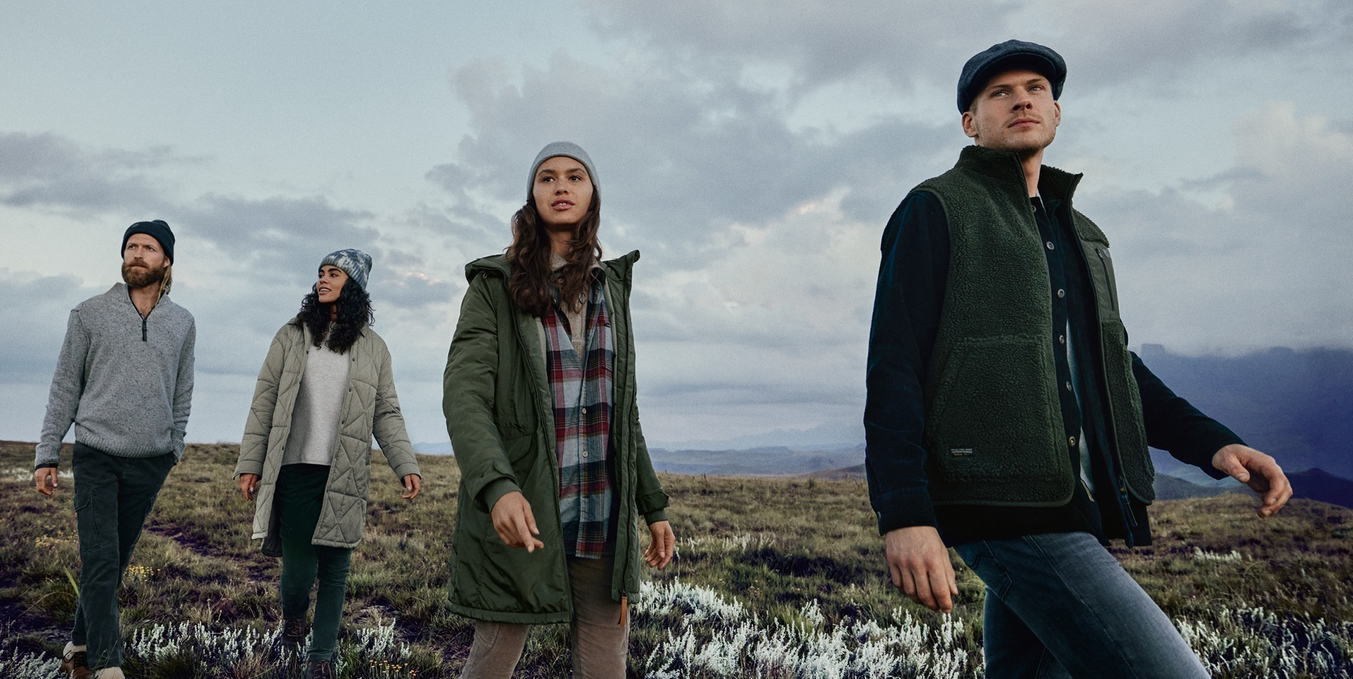 Vier Personen tragen Outdoor-Bekleidung und schauen in die Ferne, umgeben von einer Landschaft mit Wolken und Bergen. Vier Personen tragen Outdoor-Bekleidung und schauen in die Ferne, umgeben von einer Landschaft mit Wolken und Bergen.