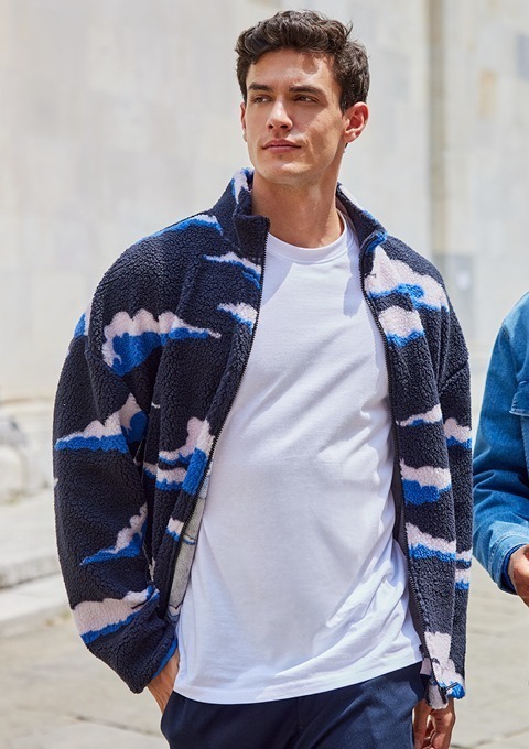 Ein junger Mann trägt eine farbige Fleecejacke mit Wolkenmuster und ein weißes T-Shirt. Ein junger Mann trägt eine farbige Fleecejacke mit Wolkenmuster und ein weißes T-Shirt.