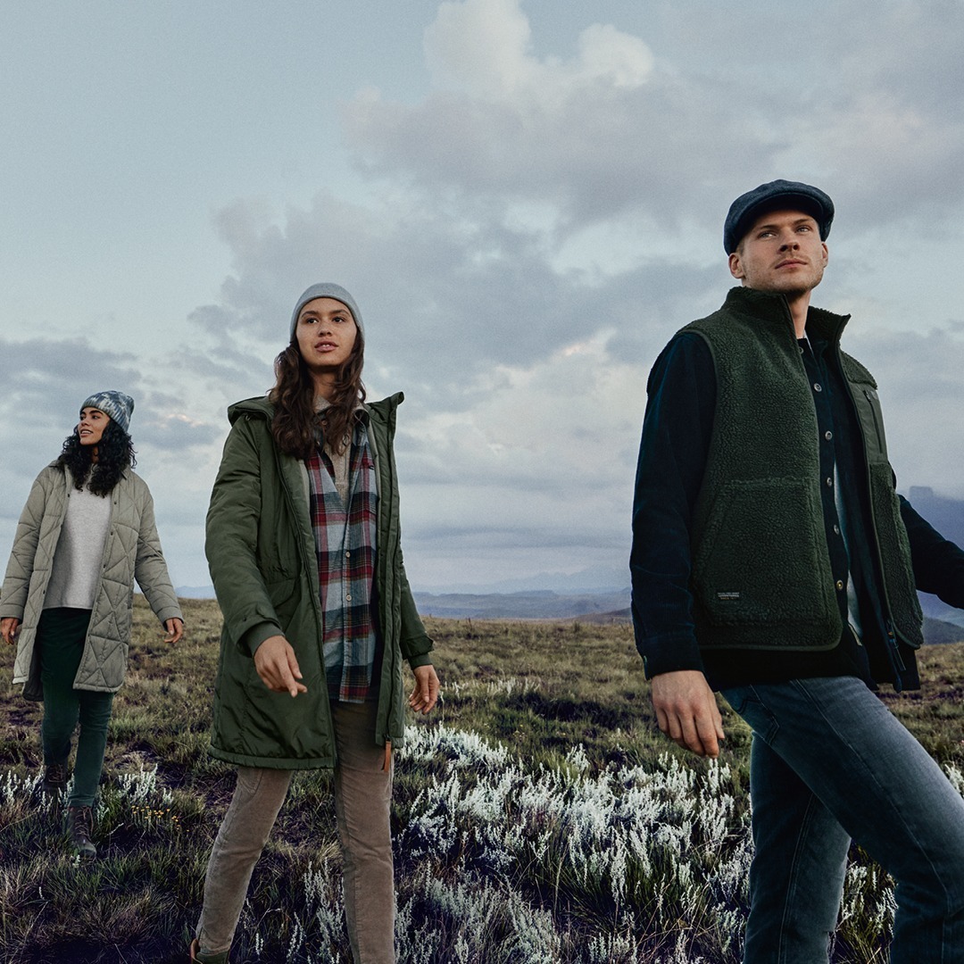 Drei Personen in warmer Kleidung stehen in einer Landschaft mit bewölktem Himmel. Drei Personen in warmer Kleidung stehen in einer Landschaft mit bewölktem Himmel.