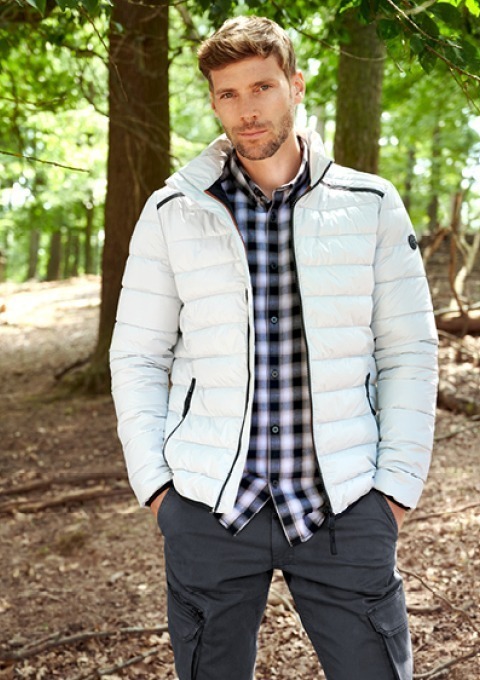 Ein Mann steht im Wald, trägt eine weiße Jacke und ein kariertes Hemd. Ein Mann steht im Wald, trägt eine weiße Jacke und ein kariertes Hemd.