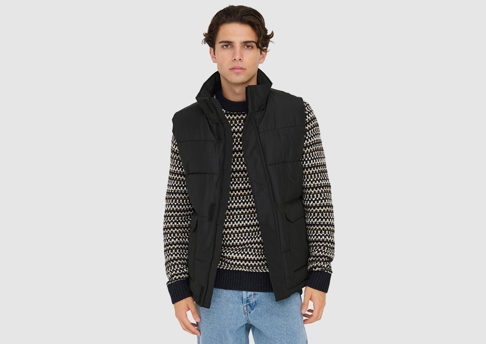 Ein junger Mann trägt eine schwarze Weste über einem gemusterten Pullover und hellen Jeans. Ein junger Mann trägt eine schwarze Weste über einem gemusterten Pullover und hellen Jeans.