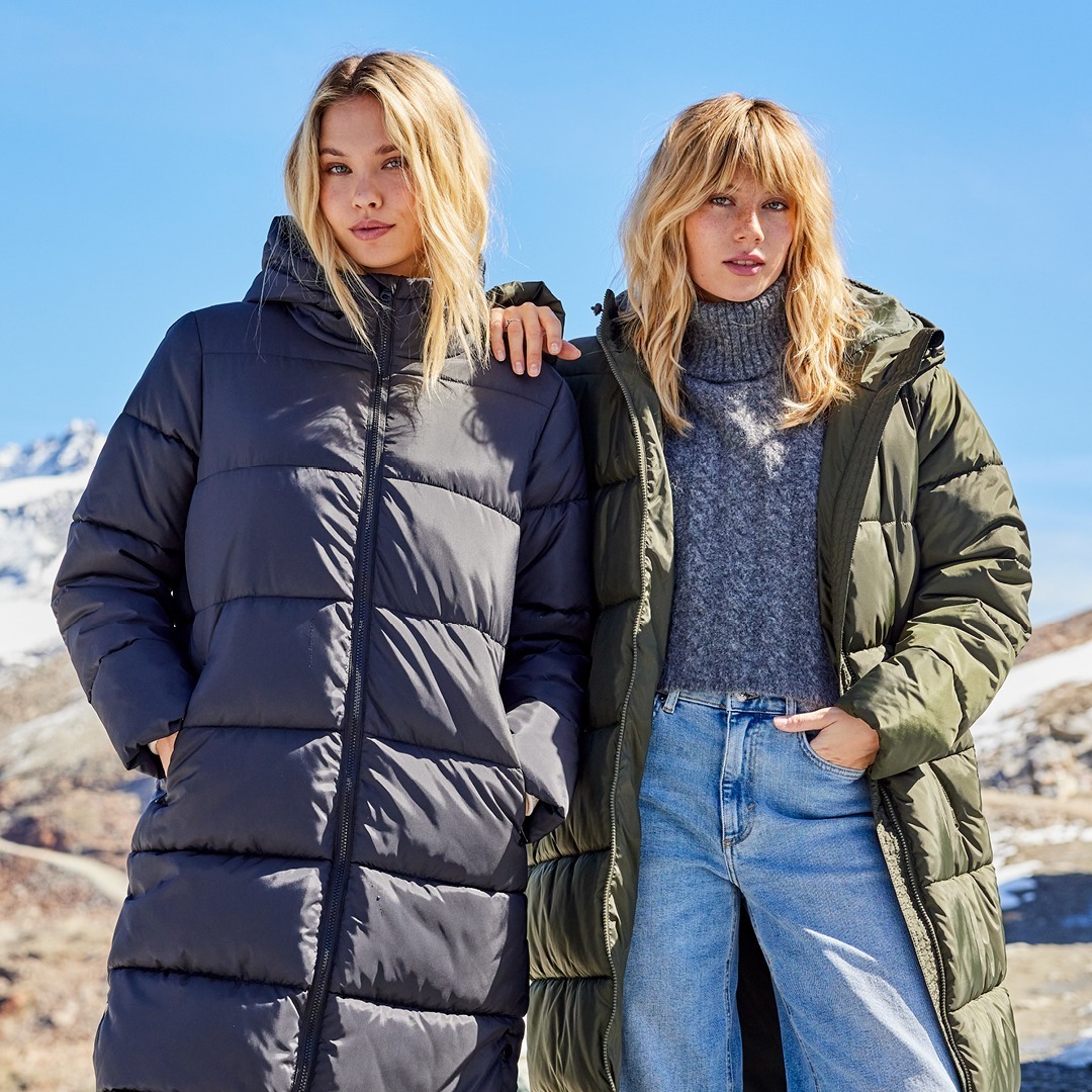 Zwei Frauen in dicken Winterjacken stehen vor einer Berglandschaft. Zwei Frauen in dicken Winterjacken stehen vor einer Berglandschaft.