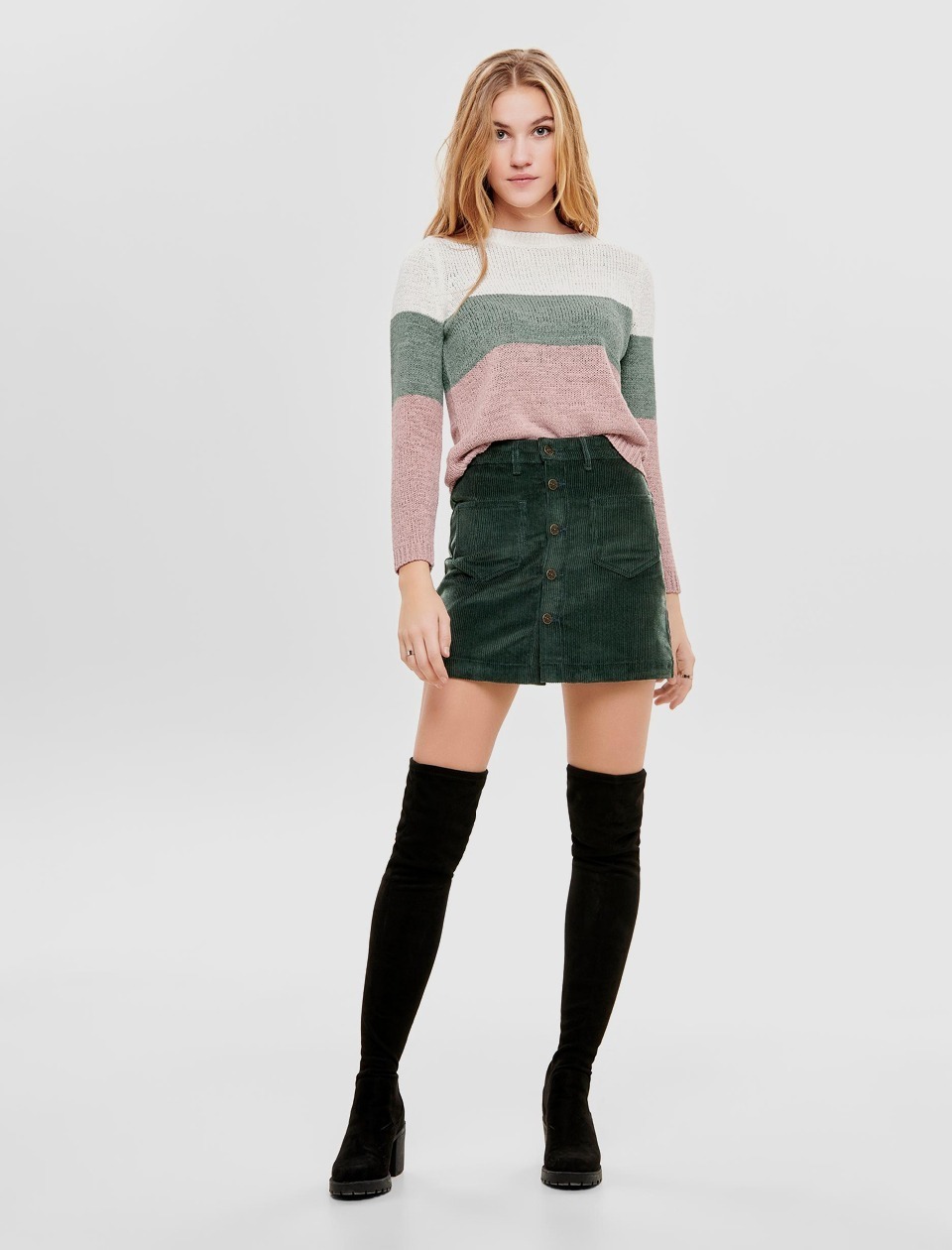 Eine Frau steht in einem gestreiften Pullover und einem grünen Rock. Sie trägt hohe schwarze Stiefel. Eine Frau steht in einem gestreiften Pullover und einem grünen Rock. Sie trägt hohe schwarze Stiefel.