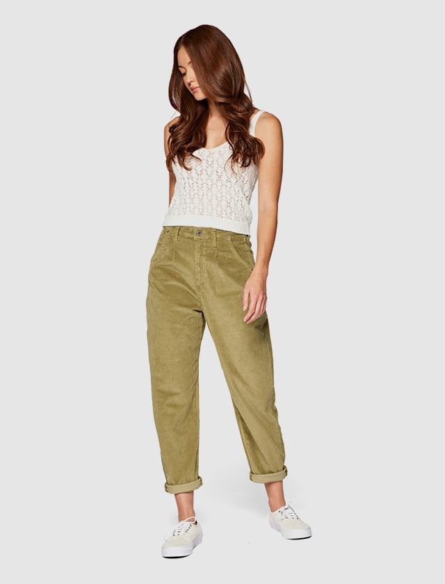 Eine Frau trägt ein weißes Top und olivgrüne Hose, mit weißen Sneakers. Sie steht aufrecht und schaut nach unten. Eine Frau trägt ein weißes Top und olivgrüne Hose, mit weißen Sneakers. Sie steht aufrecht und schaut nach unten.