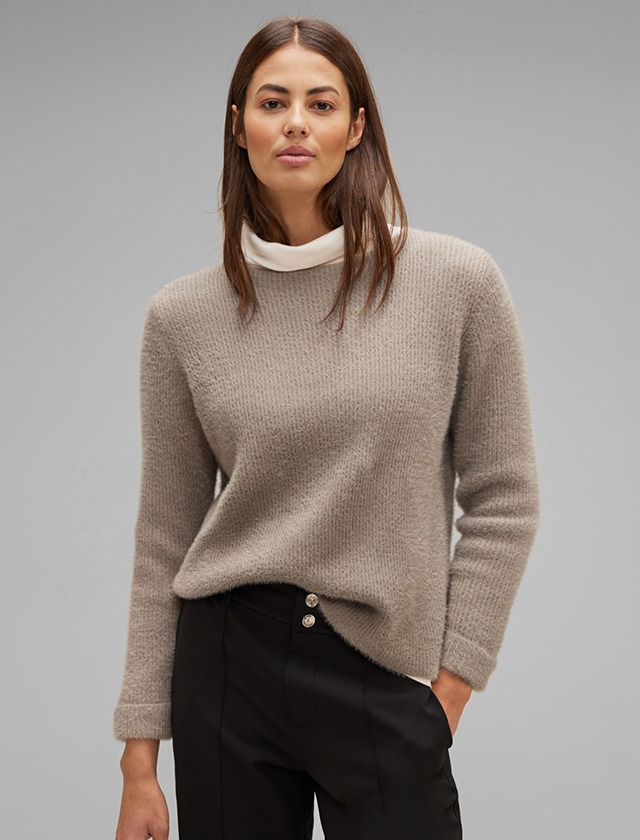 Eine Frau in einem beigen Pullover und schwarzen Hosen schaut direkt in die Kamera. Eine Frau in einem beigen Pullover und schwarzen Hosen schaut direkt in die Kamera.