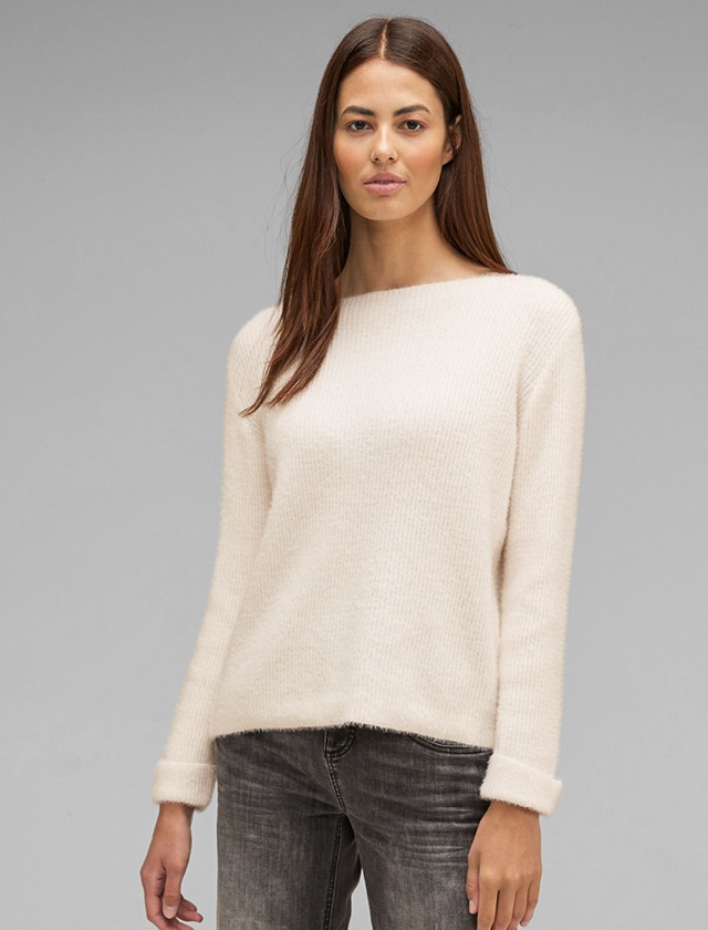 Eine Frau trägt einen hellen, flauschigen Pullover und hat lange Haare. Der Hintergrund ist grau. Eine Frau trägt einen hellen, flauschigen Pullover und hat lange Haare. Der Hintergrund ist grau.