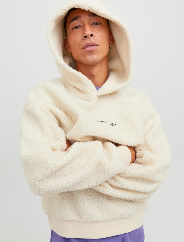 Mann in einem weißen, gefütterten Hoodie mit Kapuze, der beiläufig in die Kamera schaut. Mann in einem weißen, gefütterten Hoodie mit Kapuze, der beiläufig in die Kamera schaut.