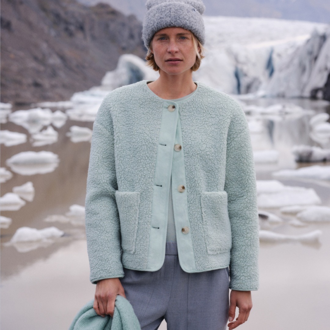 Eine Person steht vor einer eisigen Landschaft. Sie trägt eine mintgrüne Jacke und eine graue Mütze. Eine Person steht vor einer eisigen Landschaft. Sie trägt eine mintgrüne Jacke und eine graue Mütze.