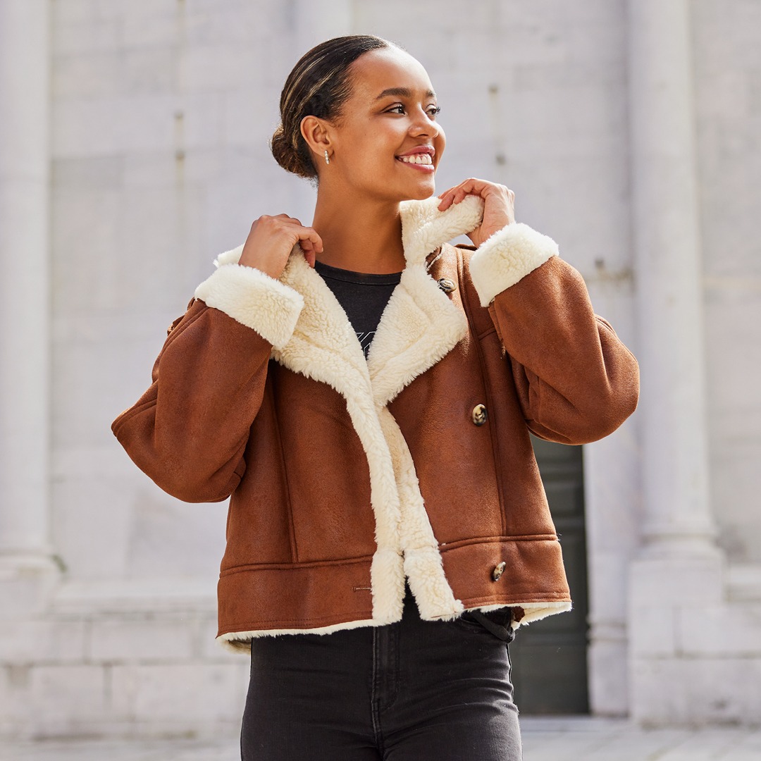 Eine Frau trägt eine braune Jacke mit weißem, pelzartigem Kragen und Lächelt. Eine Frau trägt eine braune Jacke mit weißem, pelzartigem Kragen und Lächelt.