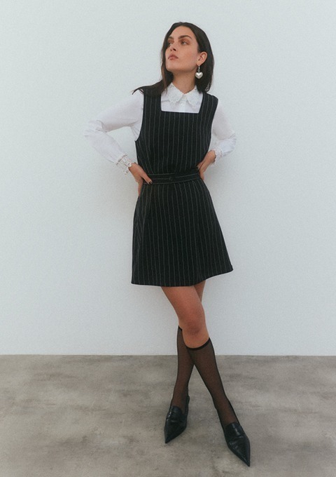 Eine Frau in einem gestreiften schwarz-weißen Kleid mit heller Bluse und hohen Schuhen steht vor einer neutralen Wand. Eine Frau in einem gestreiften schwarz-weißen Kleid mit heller Bluse und hohen Schuhen steht vor einer neutralen Wand.