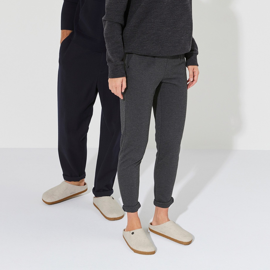 Zwei Personen in bequemen Hosen und Hausschuhen, eine in grauen und eine in dunkelblauen Hosen.