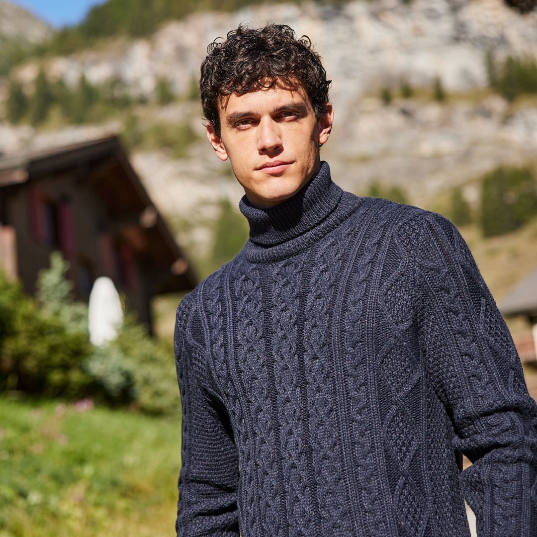 Ein Mann trägt einen dunkelblauen Rollkragenpullover und steht in einer ländlichen Umgebung mit Bergen im Hintergrund. Ein Mann trägt einen dunkelblauen Rollkragenpullover und steht in einer ländlichen Umgebung mit Bergen im Hintergrund.