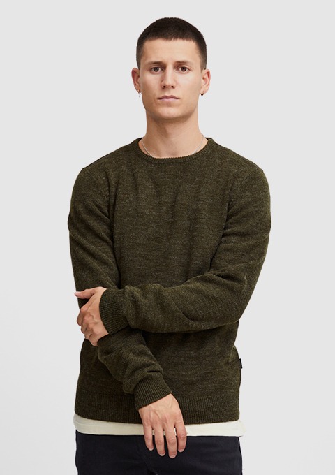 Ein junger Mann trägt einen olivgrünen Pullover und steht mit verschränkten Armen vor einem neutralen Hintergrund. Ein junger Mann trägt einen olivgrünen Pullover und steht mit verschränkten Armen vor einem neutralen Hintergrund.