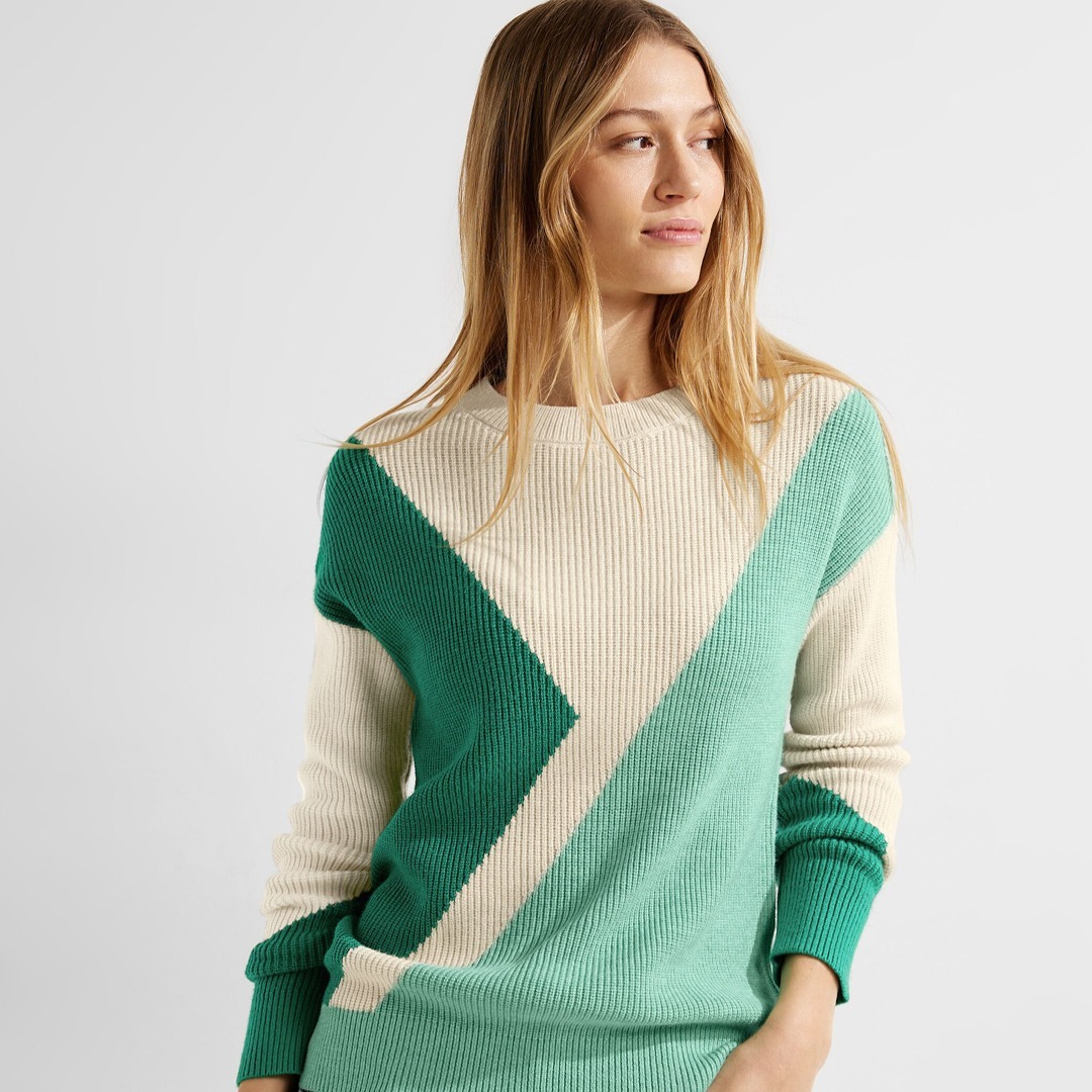 Eine Person trägt einen Pullover mit geometrischem Muster in grün und beige. Eine Person trägt einen Pullover mit geometrischem Muster in grün und beige.