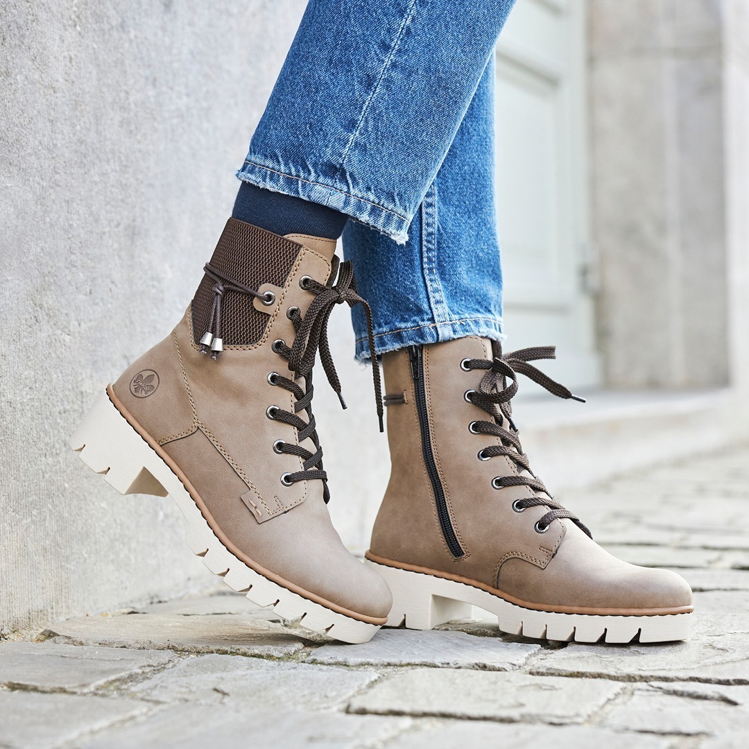 Moderne, braune Stiefel aus Leder mit weißer Sohle, getragen von einer Person in Jeans.