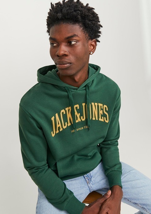Ein junger Mann trägt einen grünen Hoodie mit dem Schriftzug „JACK & JONES“. Er sitzt und schaut nachdenklich.