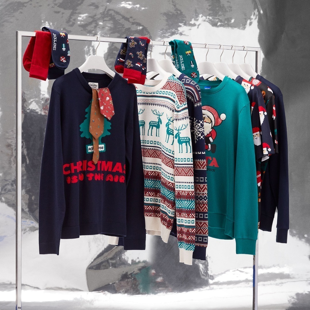 Fünf weihnachtliche Pullover und Socken hängen an einem Kleiderbügel.