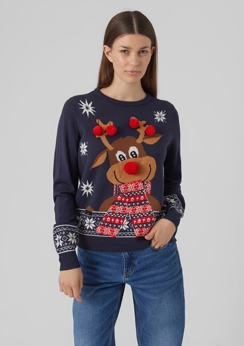 Eine Frau trägt einen blauen Pullover mit einem bunten Rentier-Motiv und Weihnachtsdekoration.