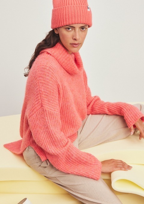 Eine Frau trägt einen pinken Pullover und eine Mütze und sitzt auf einer gelben Unterlage.