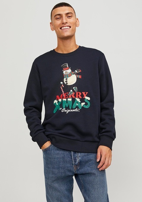 Ein lächelnder Mann trägt einen dunkelblauen Sweater mit einem Weihnachtsmann-Motiv und der Aufschrift "MERRY XMAS".