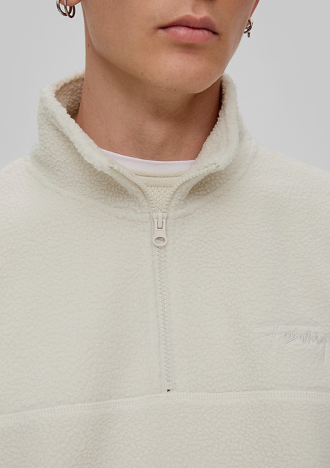 Ein junger Mann trägt einen weißen Fleece-Pullover mit halbem Reißverschluss. Ein junger Mann trägt einen weißen Fleece-Pullover mit halbem Reißverschluss.