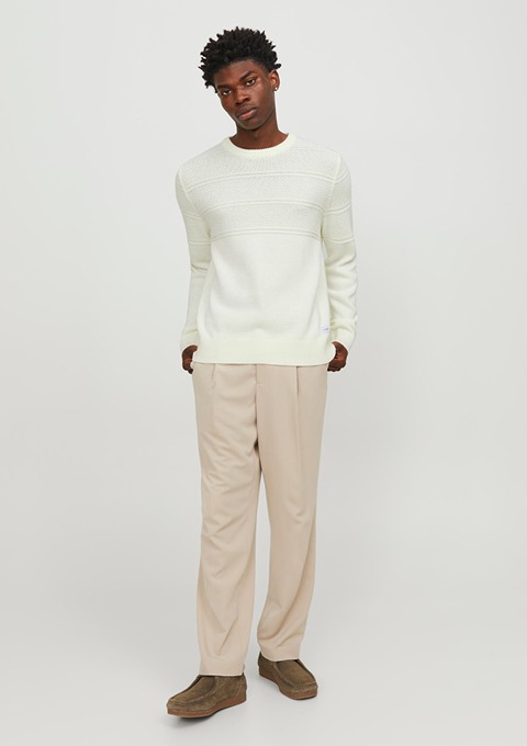 Ein Mann trägt einen hellen Pullover und beige Hosen, er steht aufrecht vor einem neutralen Hintergrund. Ein Mann trägt einen hellen Pullover und beige Hosen, er steht aufrecht vor einem neutralen Hintergrund.
