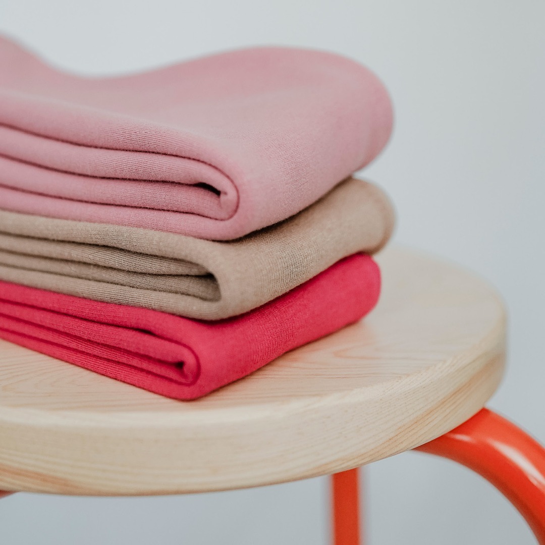 Gestapelte, gefaltete Tücher in rosa, beige und rot auf einem hölzernen Tisch. Gestapelte, gefaltete Tücher in rosa, beige und rot auf einem hölzernen Tisch.