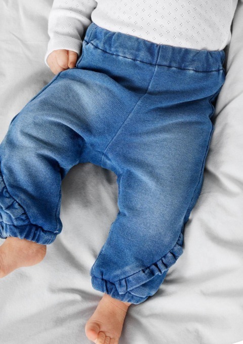 Ein Baby trägt blaue, lässige Hosen mit einem Gummizug und Rüschendetails. Ein Baby trägt blaue, lässige Hosen mit einem Gummizug und Rüschendetails.