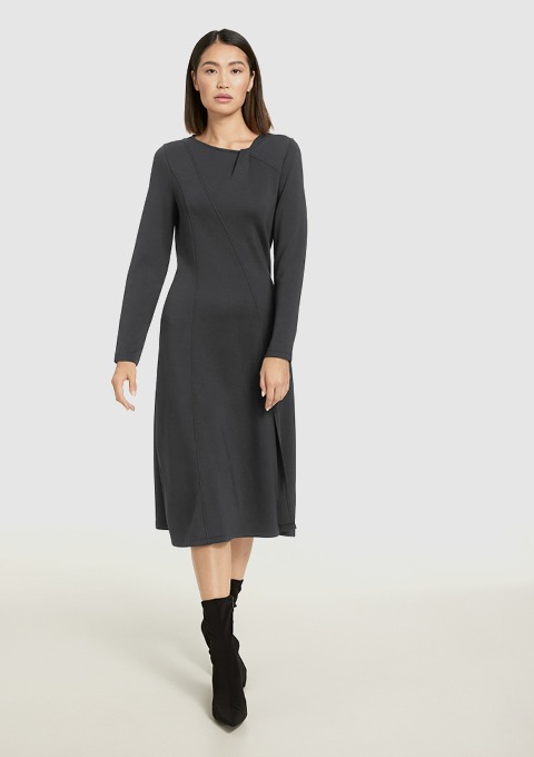 Eine Frau trägt ein langes, graues Kleid mit langen Ärmeln und schwarzen Stiefeln. Eine Frau trägt ein langes, graues Kleid mit langen Ärmeln und schwarzen Stiefeln.