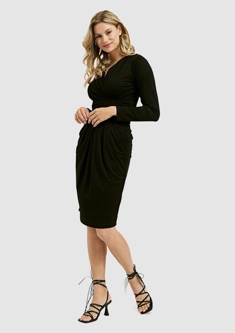 Eine Frau in einem schwarzen, langärmligen Kleid steht mit einer Hand an der Hüfte und trägt schwarze Sandalen mit hohen Absätzen. Eine Frau in einem schwarzen, langärmligen Kleid steht mit einer Hand an der Hüfte und trägt schwarze Sandalen mit hohen Absätzen.
