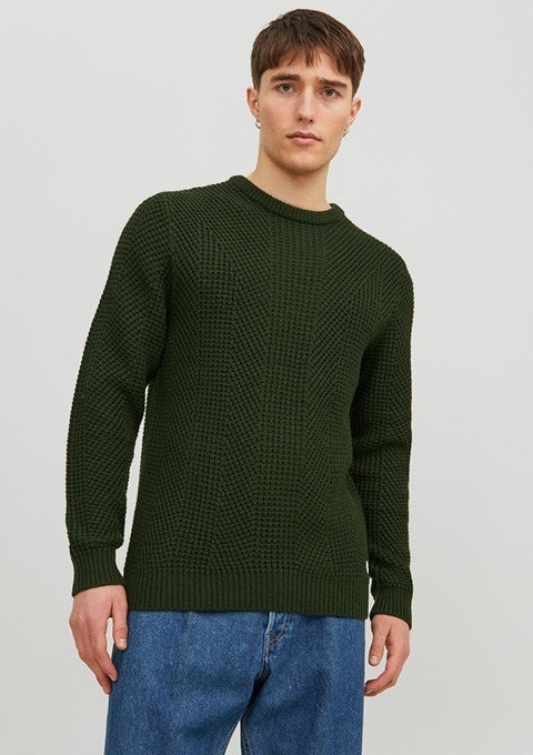 Ein junger Mann trägt einen dunkelgrünen, strukturierten Pullover und blaue Jeans. Ein junger Mann trägt einen dunkelgrünen, strukturierten Pullover und blaue Jeans.