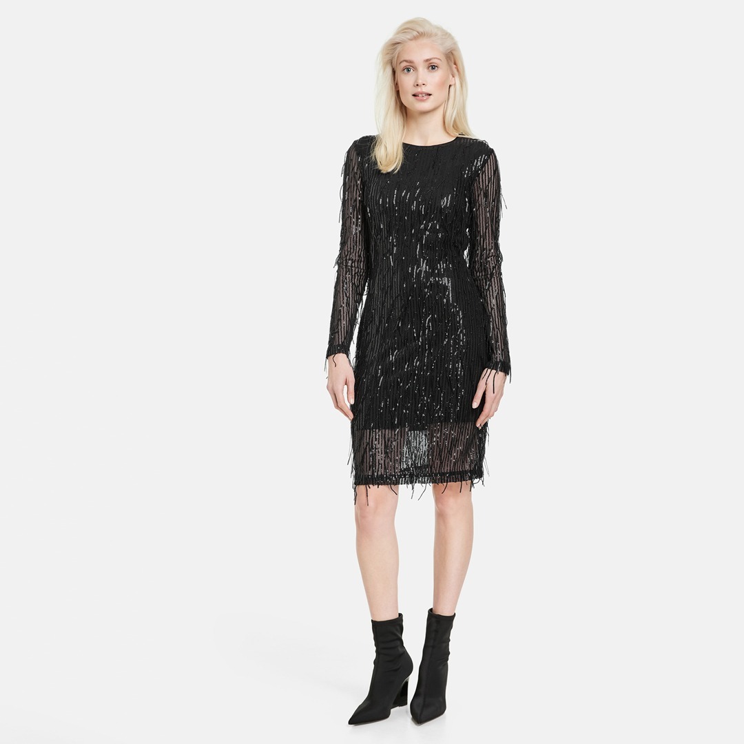 Eine Frau trägt ein schwarzes, glitzerndes Kleid mit langen Ärmeln und schwarzen Stiefeln. Eine Frau trägt ein schwarzes, glitzerndes Kleid mit langen Ärmeln und schwarzen Stiefeln.