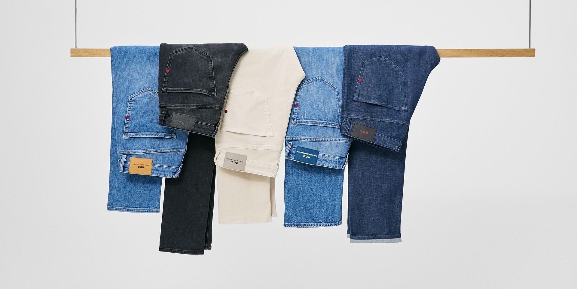 Sechs verschiedene Hosen hängen an einem Holzstange, darunter Denim- und Baumwollstoffe in verschiedenen Farben.