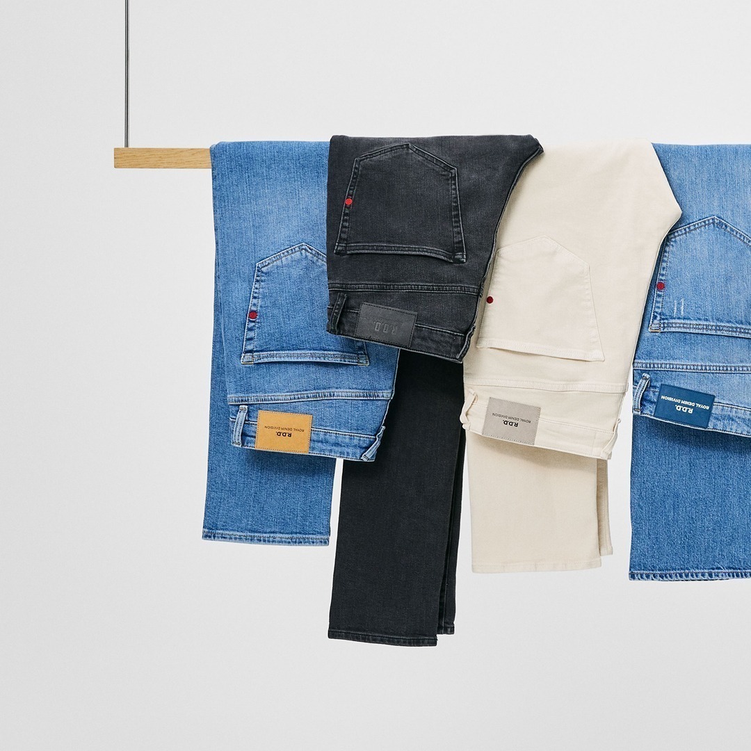 Fünf Hosen in verschiedenen Farben hängen an einem Holzstange: hellblau, dunkelblau, schwarz, beige und eine weitere hellblaue.