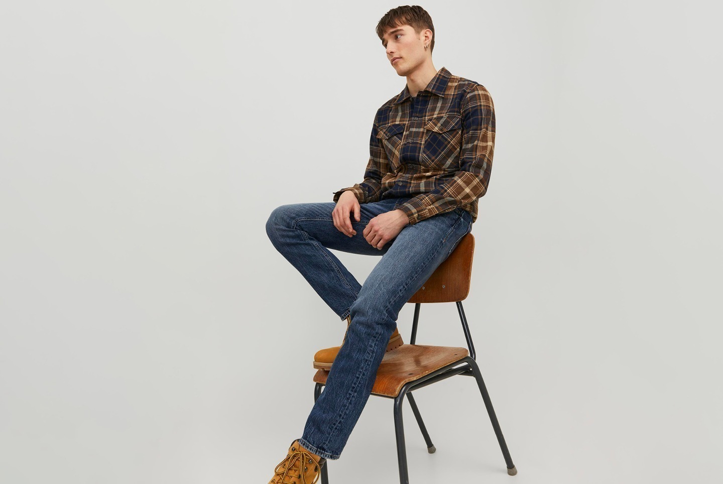 Ein Mann sitzt auf einem Holzstuhl und trägt ein kariertes Hemd und Jeans.