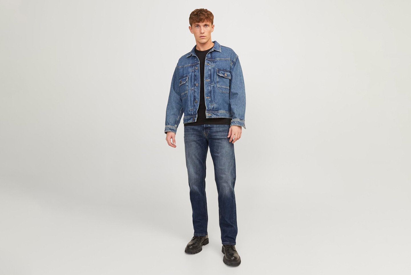 Ein Mann trägt eine Jeansjacke, ein schwarzes T-Shirt, Jeans und schwarze Schuhe.