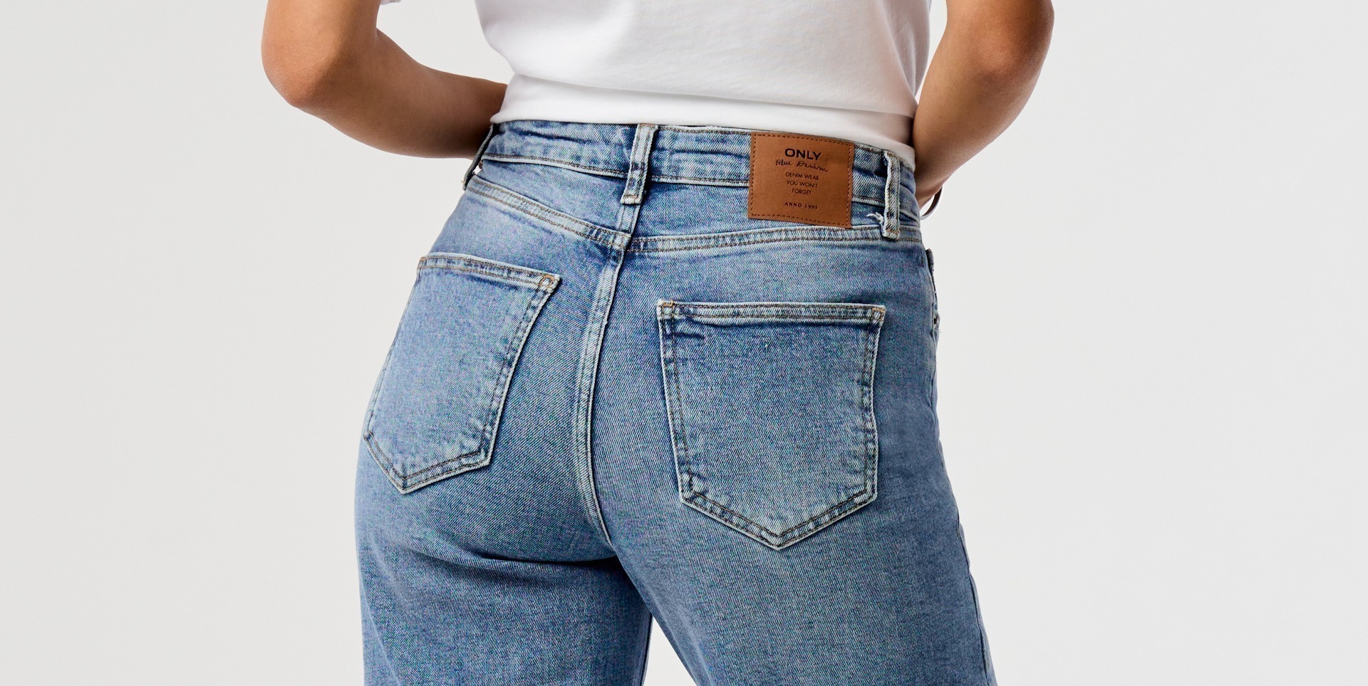 Eine Person trägt eine hellblaue Jeans von hinten, mit einem braunen Etikett am Bund. Eine Person trägt eine hellblaue Jeans von hinten, mit einem braunen Etikett am Bund.