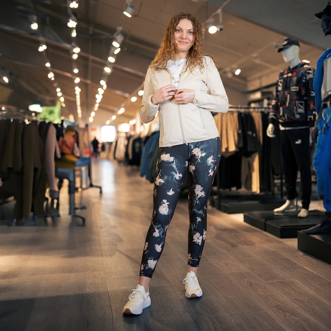 Eine Person steht in einem Geschäft, trägt eine helle Jacke, ein T-Shirt und leggings mit floralem Muster.