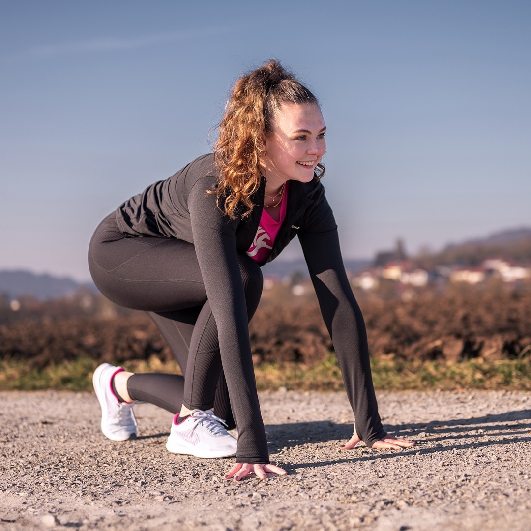 Eine sportliche Person in Sportkleidung macht eine Startposition auf einem Kiesweg.