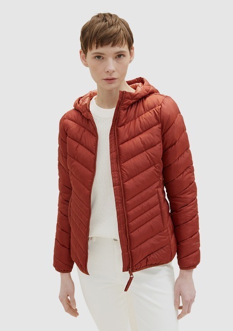 Eine Person trägt eine rote, gesteppte Jacke mit Kapuze und einem weißen Pullover darunter.