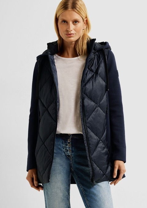 Eine Frau trägt eine dunkelblaue Jacke mit Kapuze und einem weißen T-Shirt, kombiniert mit Jeans.