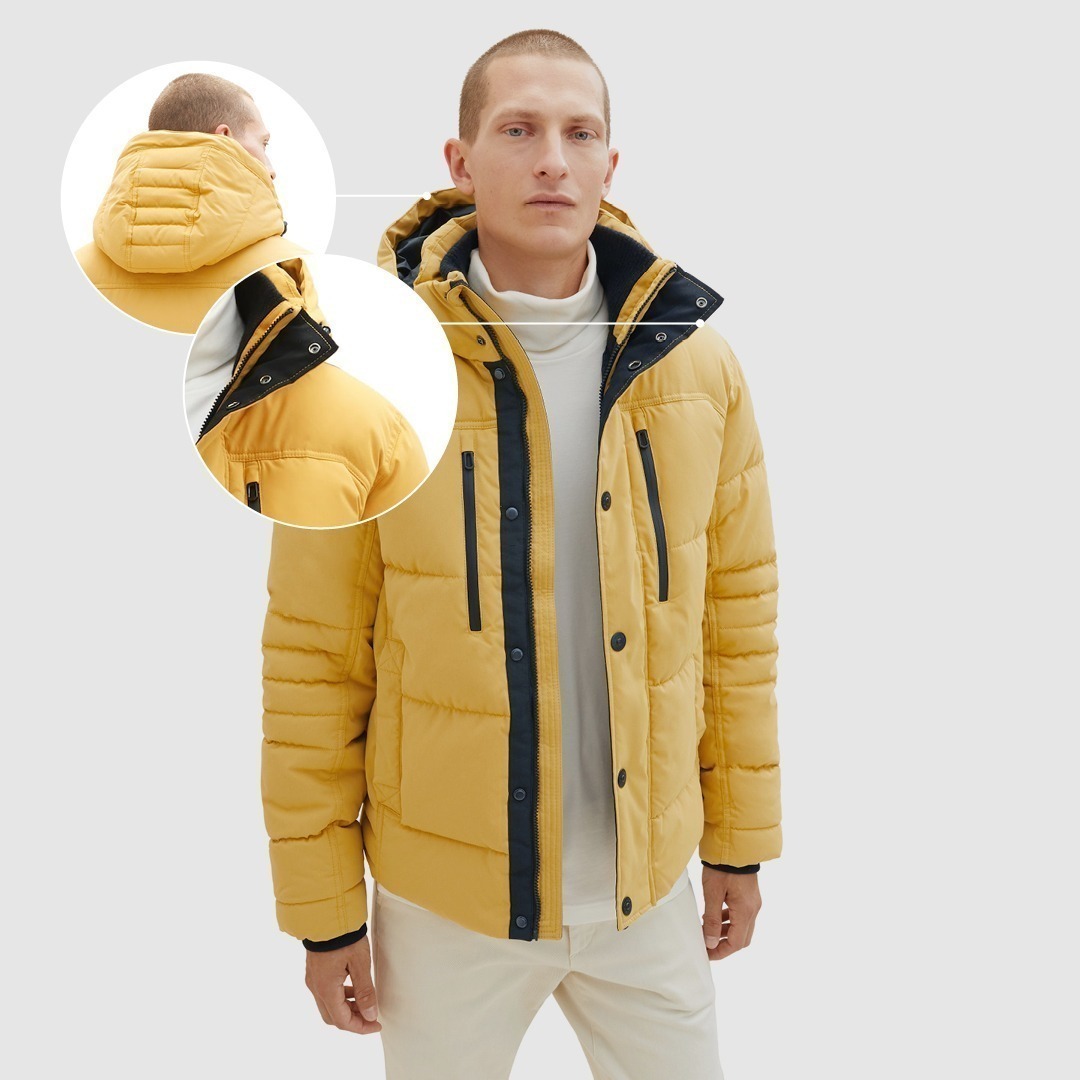 Eine gelbe, gepolsterte Jacke mit Kapuze, getragen von einem Mann.