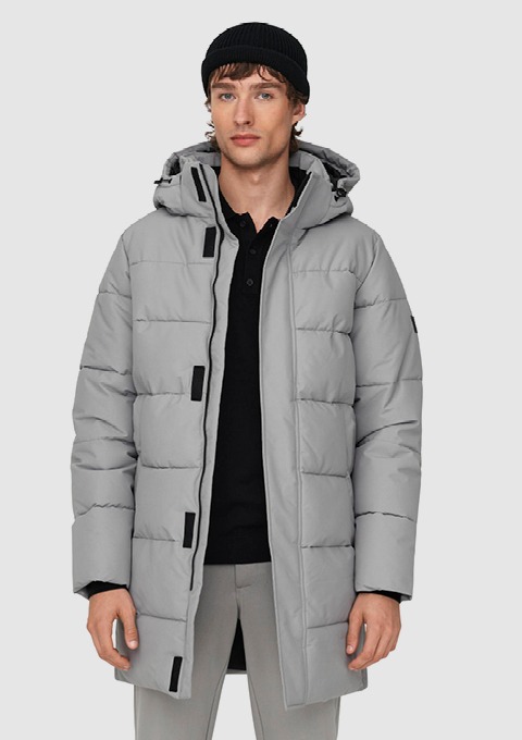 Ein junger Mann trägt eine graue, gepolsterte Winterjacke mit Kapuze und einem schwarzen Pullover darunter.