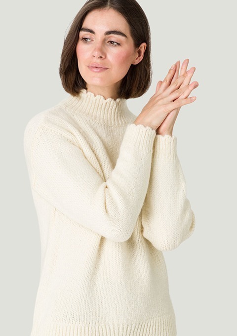 Eine Frau in einem weißen Pullover mit hohem Kragen, die ihre Hände vor sich faltet. Eine Frau in einem weißen Pullover mit hohem Kragen, die ihre Hände vor sich faltet.
