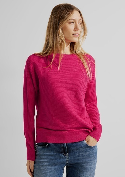 Eine Frau trägt einen pinken Pullover und Jeans.